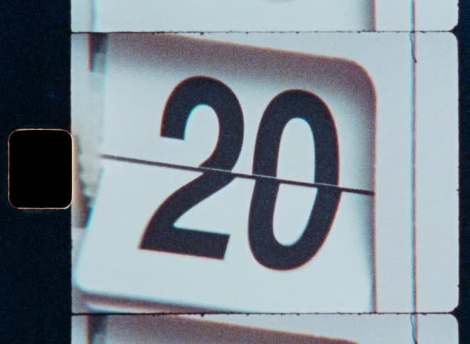 A close-up shot of a retro flip calendar counting through the days of the month from 1 to 31, captured on grainy vintage film