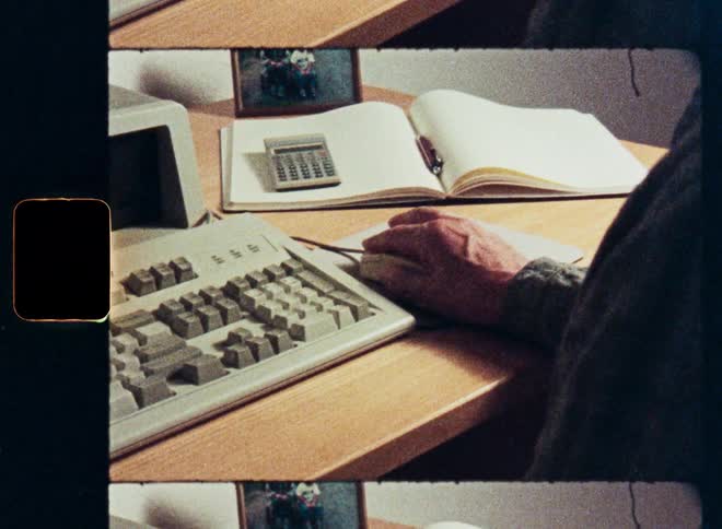 Close-up of a person's hand using an old computer mouse while working at a vintage desk with a keyboard and calculator