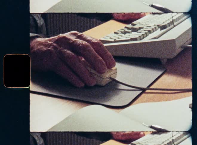 Archival film scan shows a close-up of hands using a vintage computer mouse and keyboard from the 1990s