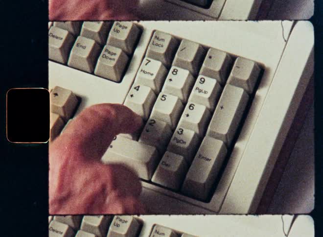 A close-up of a person typing on the number pad of a vintage computer keyboard, captured with a retro film strip aesthetic