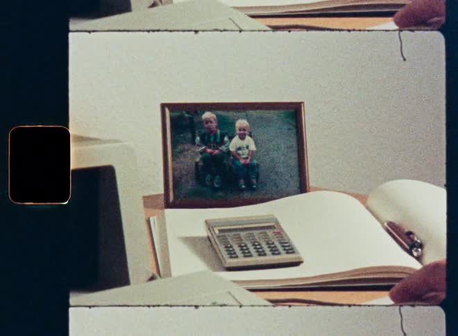 Super 8 footage shows a person working on an old computer in an office with a family photo on the desk