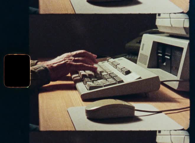 Vintage film footage shows a close-up of a person's hands typing on a retro computer keyboard