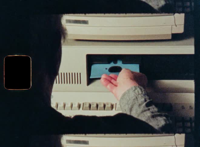Vintage footage from the 1980s shows a person inserting a floppy disk into an old personal computer