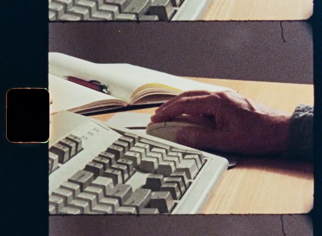 Vintage 8mm footage captures a close-up of a person's hands typing on an old computer keyboard and using a mouse