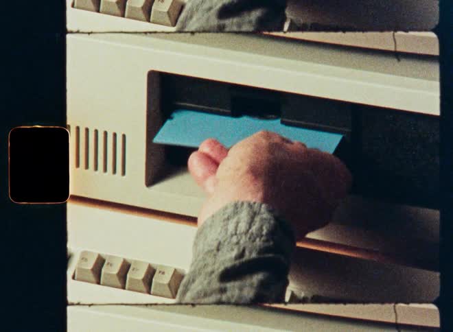 A kaleidoscopic close-up of a hand inserting a blue floppy disk into a vintage computer drive