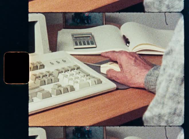 Close-up of a hand using a vintage computer mouse and keyboard on a desk in archival 80s style footage