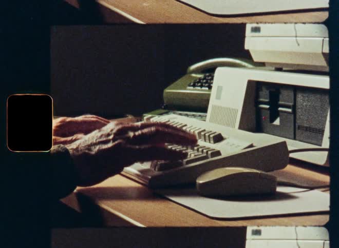 Authentic film footage shows a close-up of hands typing on a vintage 1980s computer keyboard