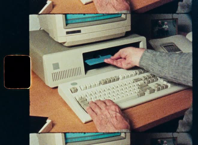 A person's hands insert a blue 5.25-inch floppy disk into an old desktop computer and then type on the keyboard