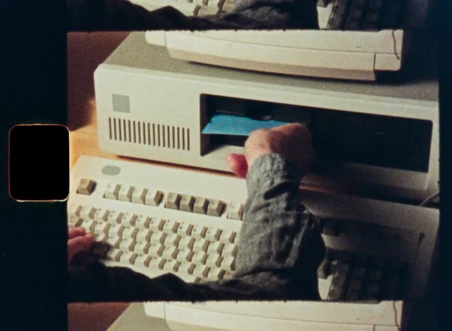 Vintage film footage shows a person inserting a floppy disk into an old desktop computer and typing on the keyboard