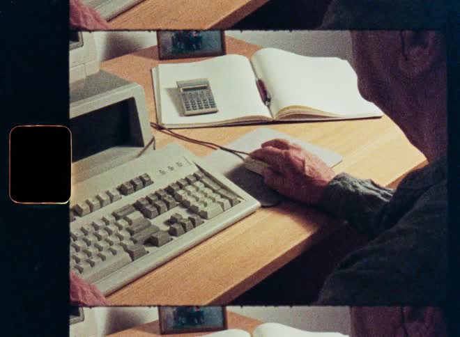 Vintage film footage captures an older man's hands typing on a retro computer keyboard and using a mouse