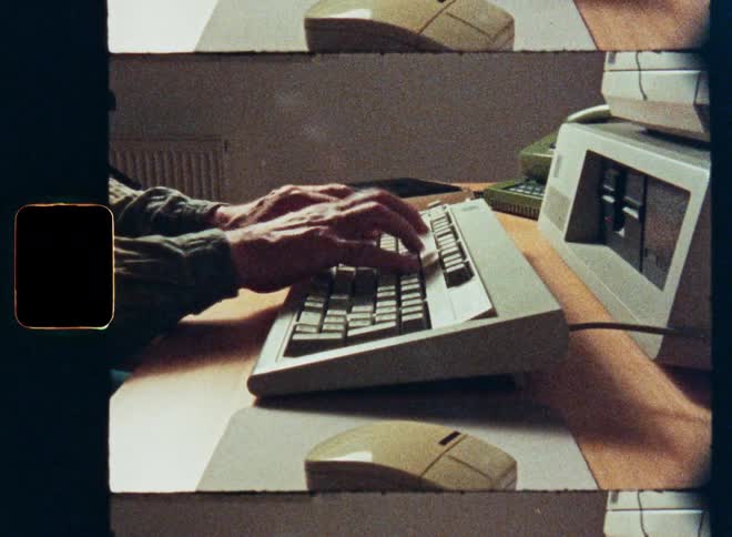 Vintage 16mm film footage of a person working and typing on a retro desktop computer from the 80s or 90s