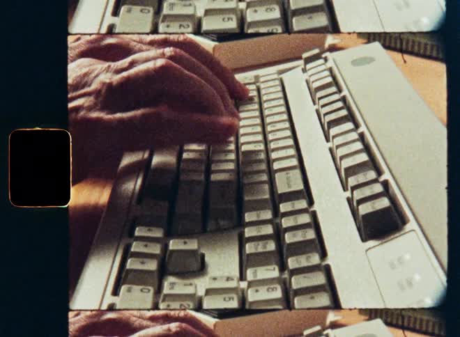 Authentic film scan shows a close-up of hands typing on a vintage computer keyboard and mouse