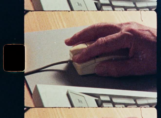 Close-up archival shot of a hand clicking an old, vintage computer mouse on a desk with a film aesthetic