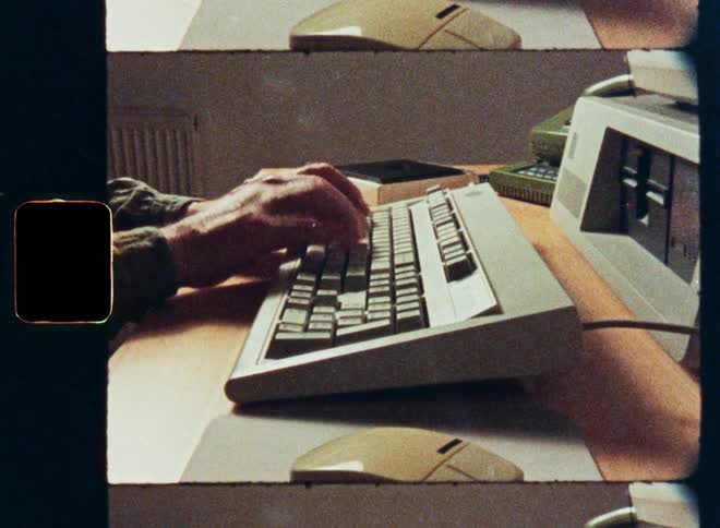 A close-up shot of a person's hands typing on an old-fashioned computer keyboard from the 1980s or 90s, captured on grainy vintage film