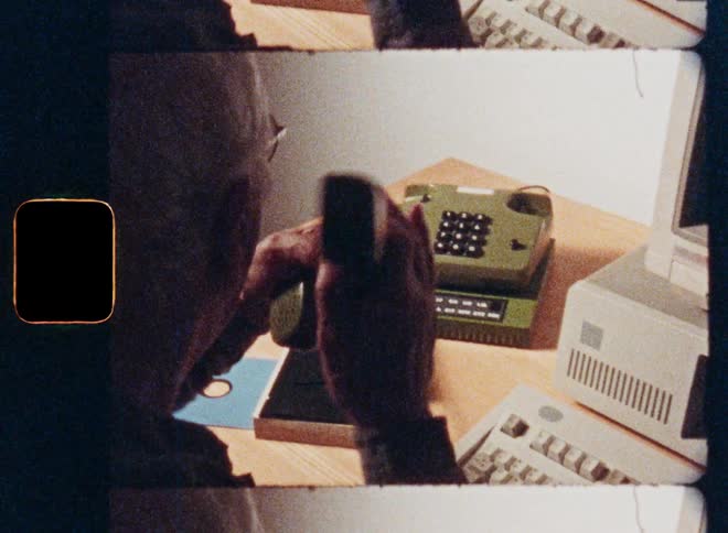 Archival film look of a person typing on a vintage 1980s computer before answering a retro telephone