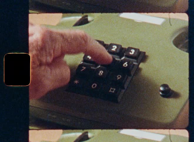 A close-up shot of a hand dialing a phone number on a vintage, olive green push-button telephone from an archival film scan