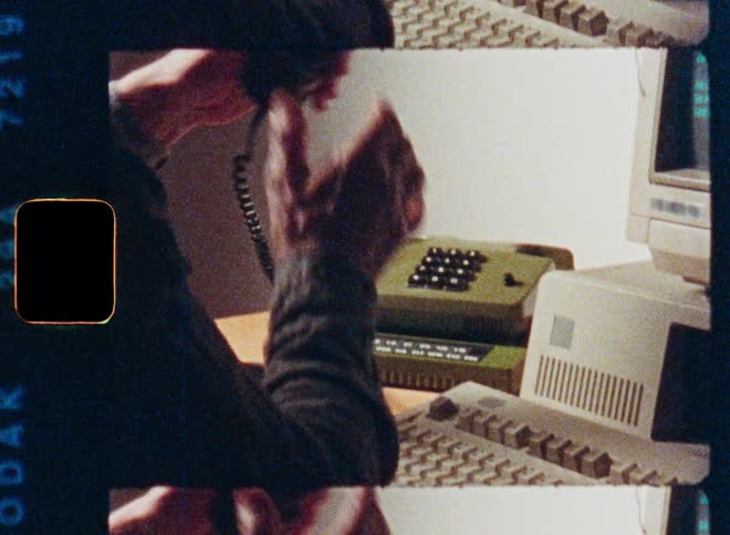Vintage 8mm film captures a person typing on an old computer before answering a green push-button telephone at their desk