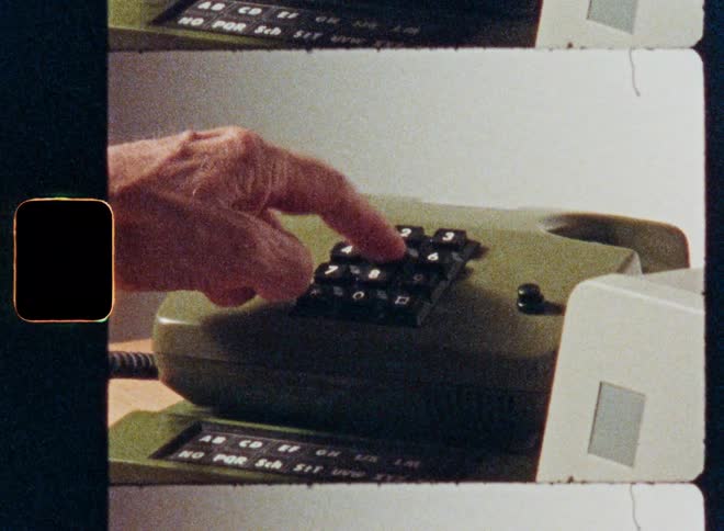 Archival film scan shows a hand picking up the receiver and dialing a number on a vintage push-button telephone