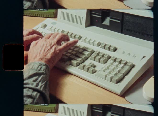 Close up of an older person's hands typing on an old vintage computer keyboard from the 1980s or 90s