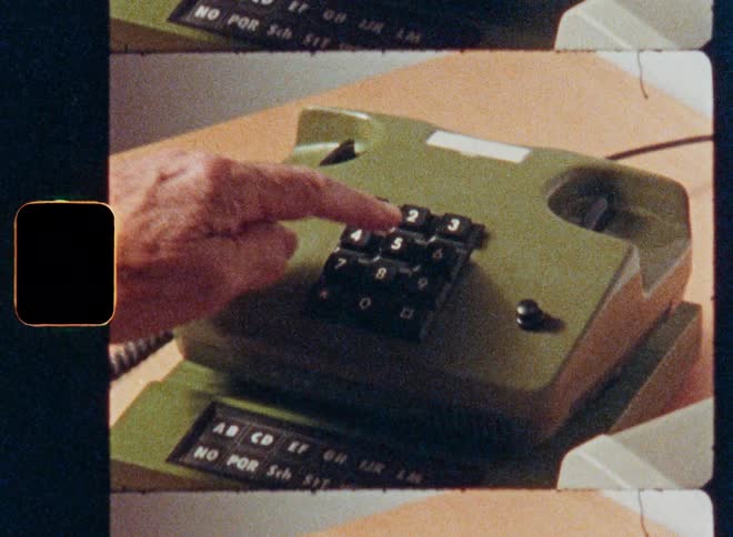 A close-up of a hand picking up and dialing a number on a vintage green push-button telephone, captured on archival film