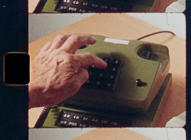 Close-up archival film footage of a hand picking up the receiver and dialing a number on a vintage green push-button telephone