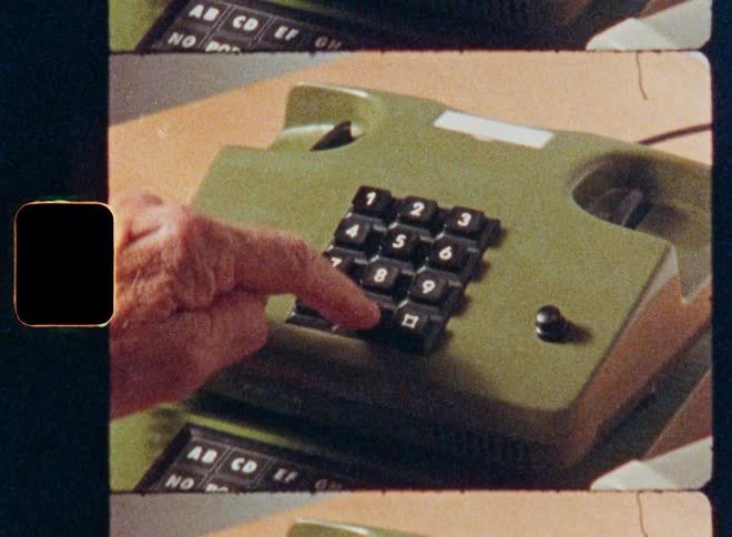 Close-up shot on vintage film of a hand picking up and dialing a number on a retro green push-button phone