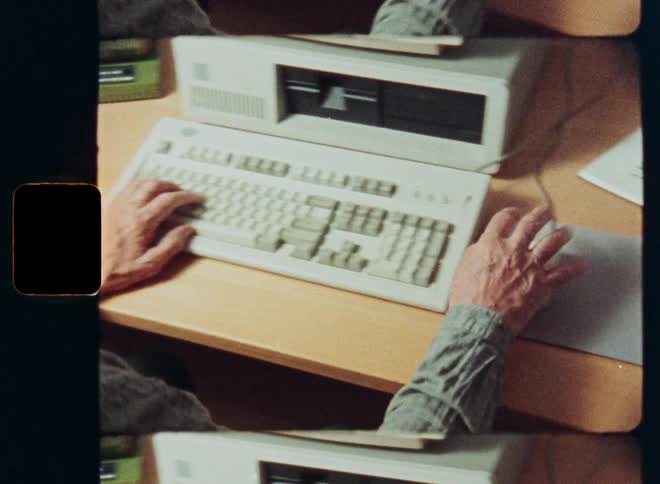 Vintage footage from the 1980s shows a person working on an early personal computer at their desk