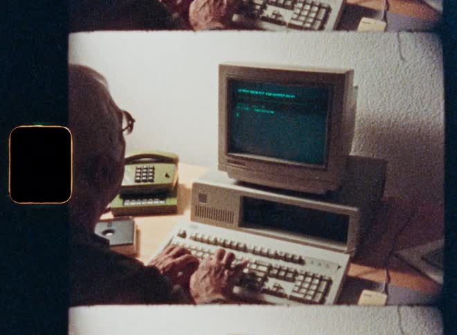 Authentic vintage footage shows an elderly man from behind, programming on an old personal computer from the 1980s