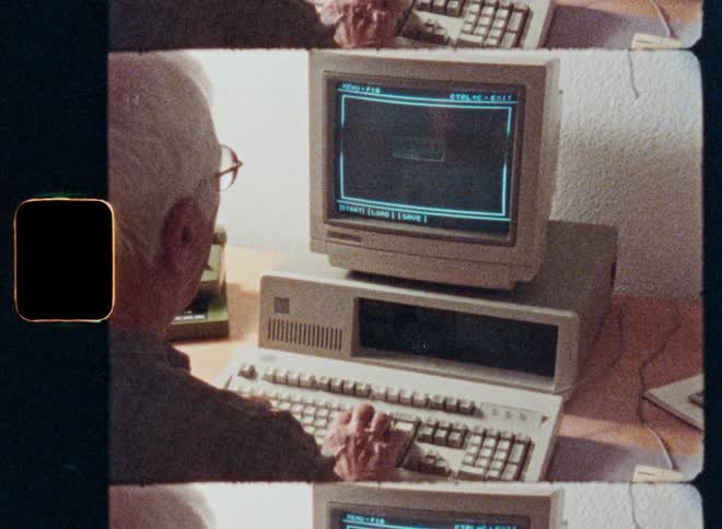 Vintage film footage shows an elderly man with white hair typing on a classic 1980s personal computer