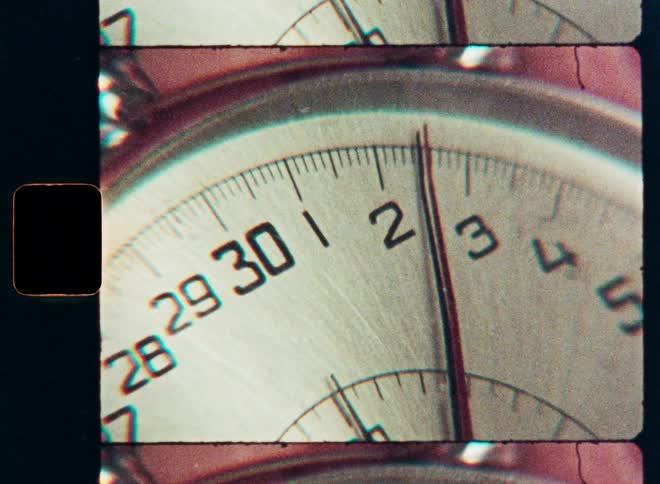 A macro, vintage film scan of a stopwatch's second hand ticking and counting time