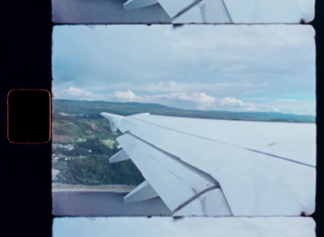 Authentic 8mm film captures an airplane wing as it flies over a lush, green coastal landscape