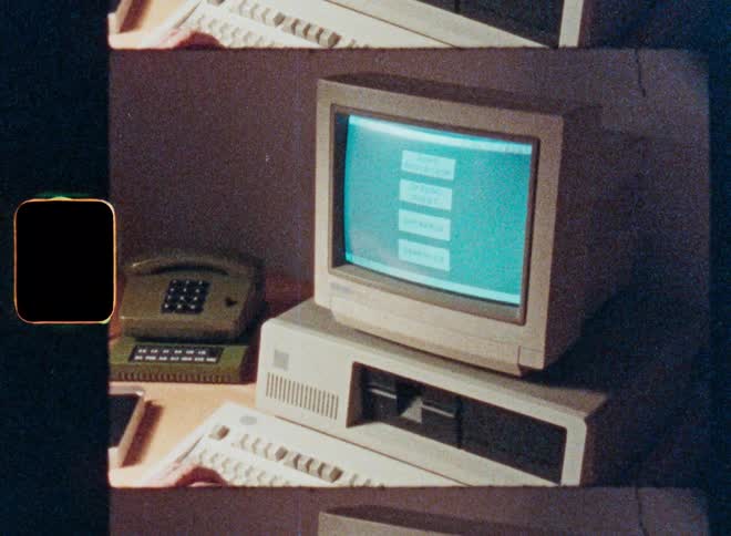 Grainy film footage shows a person typing on a vintage 1980s personal computer with a green screen monitor