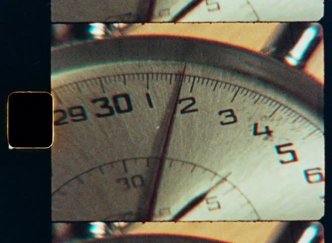 A close-up of a vintage stopwatch counting seconds, captured on old film with visible sprocket holes and grain