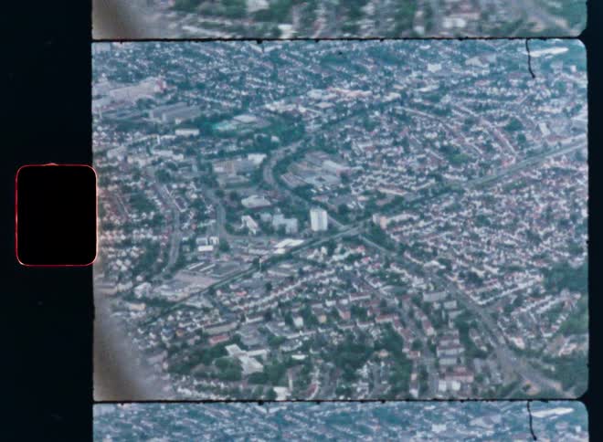 A shaky, vintage 8mm aerial view looking down on a sprawling cityscape with roads and buildings