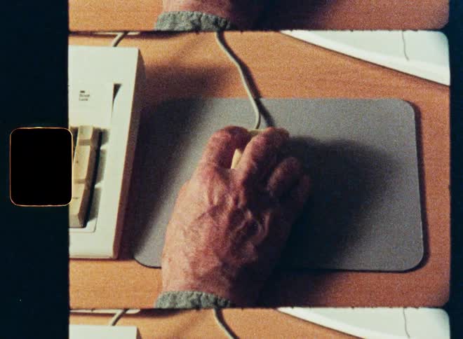 Overhead shot on vintage film of a hand using an old, single-button computer mouse on a desk