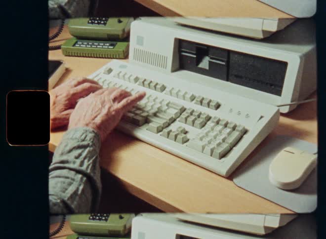 Super 8mm film style footage of an elderly person's hands typing on a vintage desktop computer from the 1980s