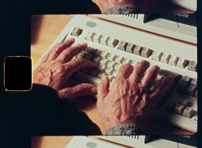 A man types on a vintage computer keyboard in an old office setting, shot on 8mm film