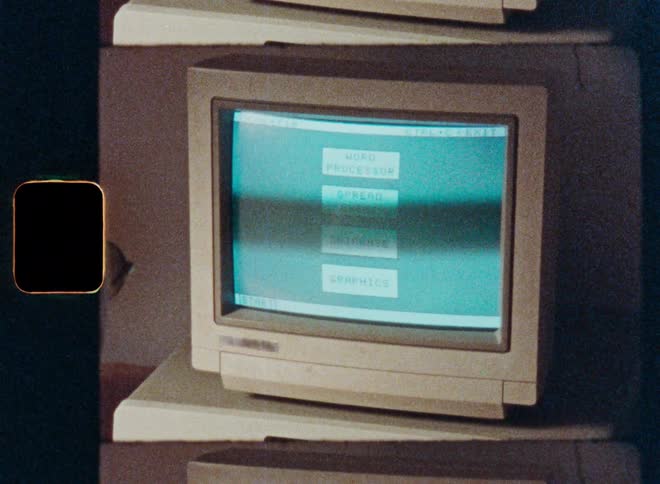 A person types on a vintage 1980s computer keyboard and navigates an old software menu on a CRT monitor, captured on grainy, stylized film