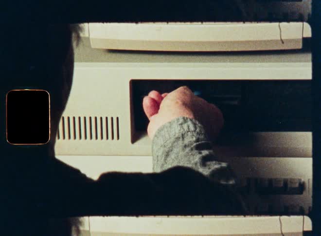 A person removes a blue floppy disk from a vintage 1980s computer system