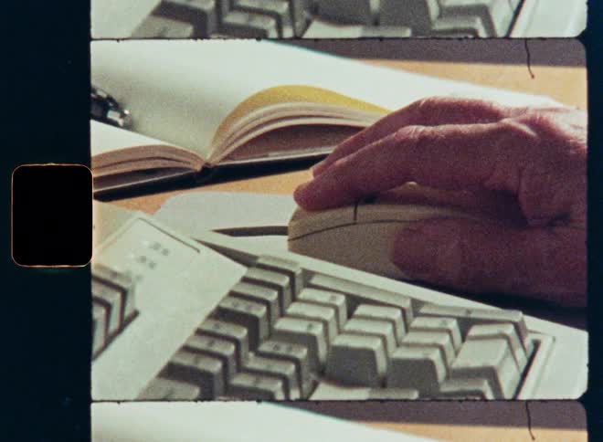 Vintage film captures a close-up of a hand using an old computer mouse and keyboard from the early days of personal computing