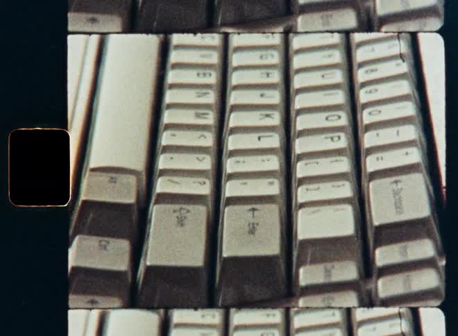 A grainy, old film close-up pans slowly across the keys of a vintage computer keyboard