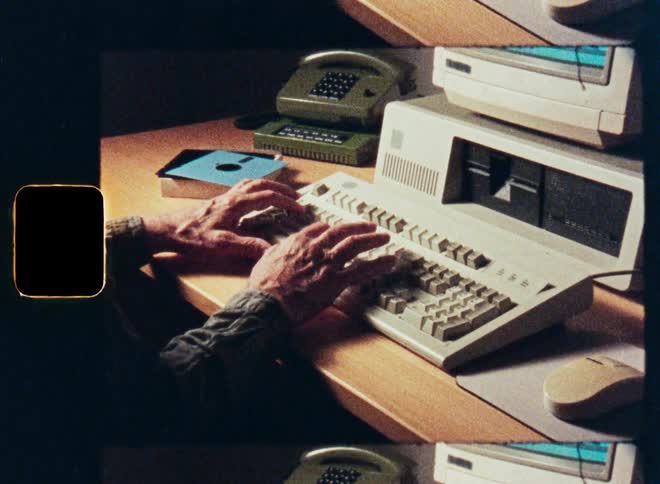 Hands of a person typing on a vintage 1980s desktop computer in an office, scanned from old film