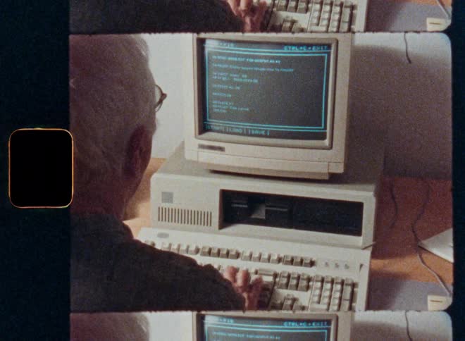 A retro film scan shows an elderly man with white hair typing on a vintage 1980s personal computer