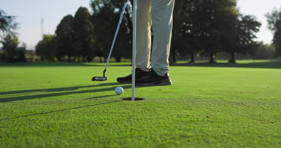 Low angle slow motion shot of a golfer putting on a green, missing the hole