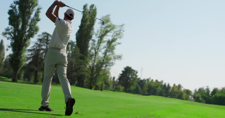 Slow motion shot of a male golfer taking a powerful swing on a beautiful, sunny golf course