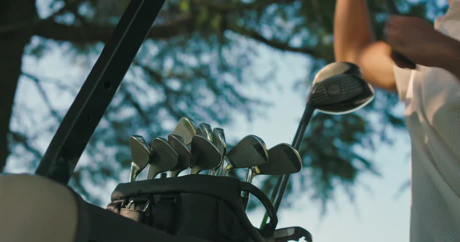 Low-angle close-up of a golfer selecting an iron from his golf bag on the course