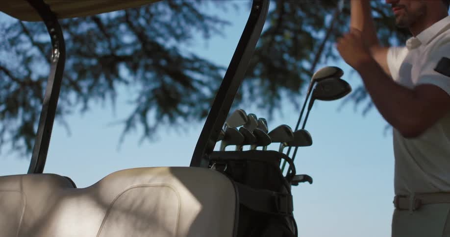 A handsome golfer selects a club from his bag on a golf cart in slow motion on a sunny day