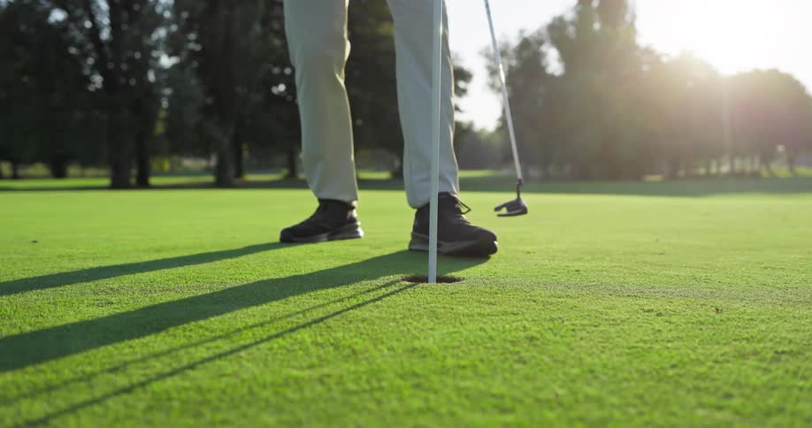 A golfer sinks a putt on a beautiful sunny green in slow motion and retrieves the ball from the hole