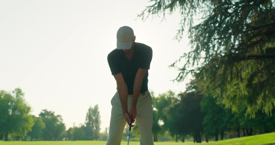 A silhouetted golfer takes a perfect swing in slow motion against the bright morning sun on a beautiful golf course