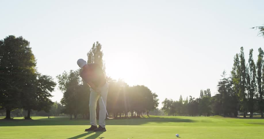 A male golfer in a slow-motion tracking shot putts a golf ball across the green on a sunny day